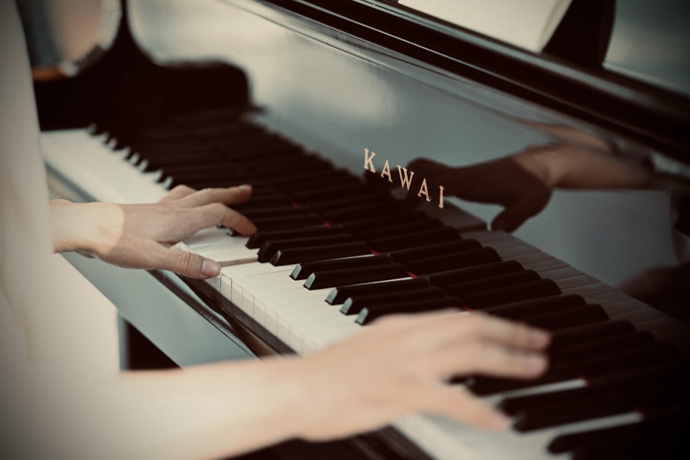 A student's hands playing a glossy black Kawai grand piano